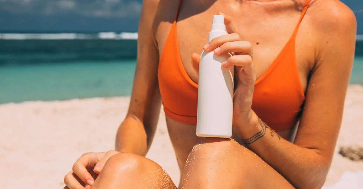 Mujer aplicando protector solar en una playa soleada, enfatizando la protección de la piel y el ambiente veraniego.
