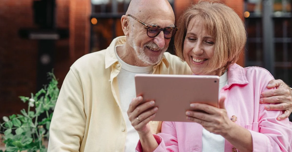 Feliz pareja de ancianos usando una tableta juntos, disfrutando del tiempo de ocio al aire libre.