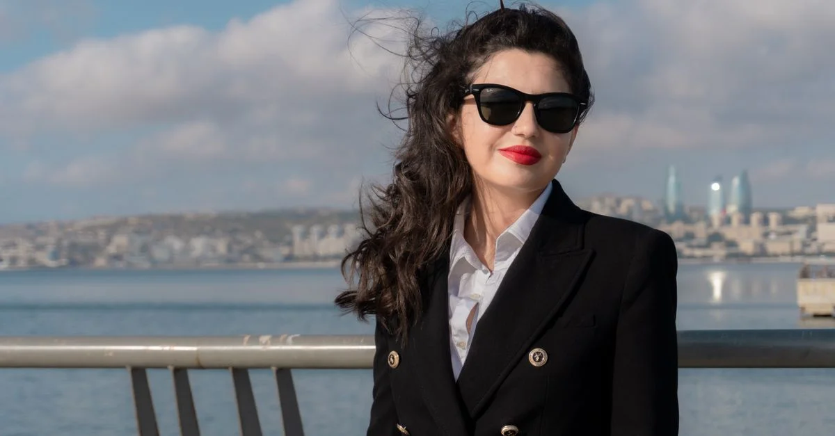 Una mujer elegante con gafas de sol posa frente al horizonte y el paseo marítimo de Bakú.
