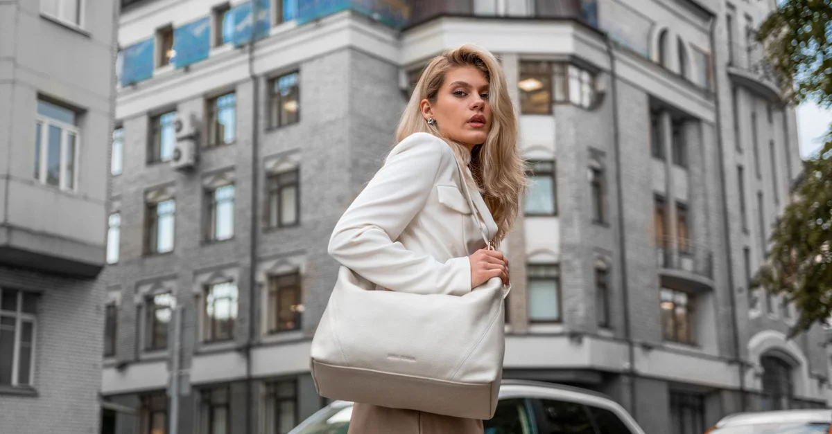 Mujer elegante en un atuendo blanco y bolsa caminando por la calle de la ciudad.