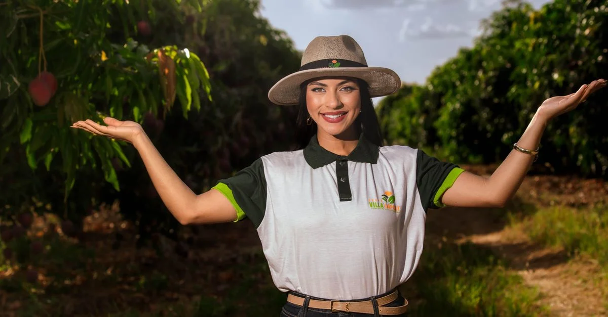 Una mujer alegre con sombrero está en un exuberante huerto de mangos, dando la bienvenida a la temporada de cosecha.
