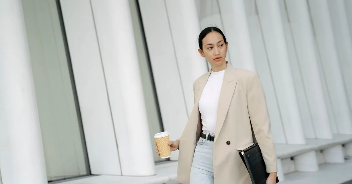 Mujer segura con cabello oscuro hace una pausa para café fuera de un edificio de oficinas.