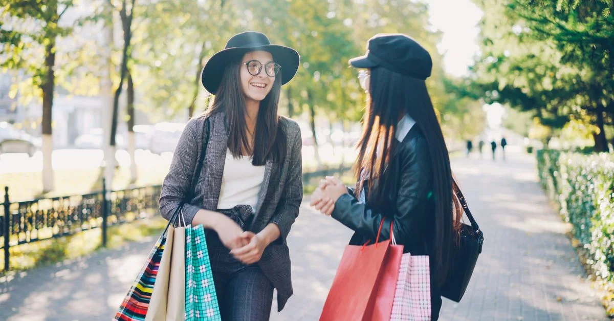 Dos mujeres elegantes con bolsas de compras sonríen al aire libre en un día soleado.