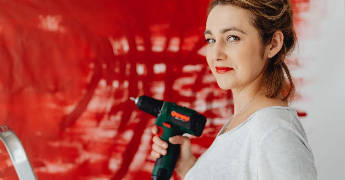 Mujer utilizando un taladro frente a una pared pintada de rojo, mostrando empoderamiento.