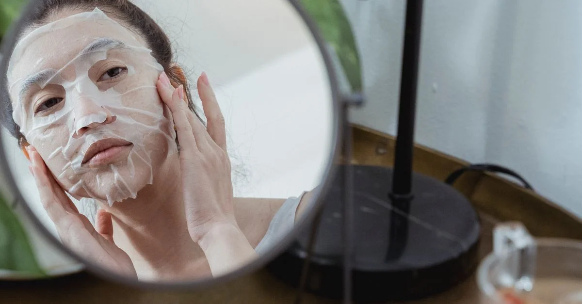 Una mujer aplica una máscara facial mientras mira su reflejo en un espejo para el cuidado de la piel.