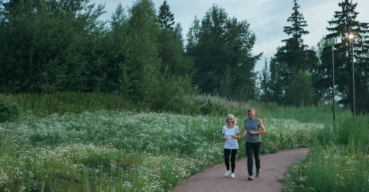 Pareja de ancianos trotando por un pintoresco sendero en el parque rodeado de vegetación.
