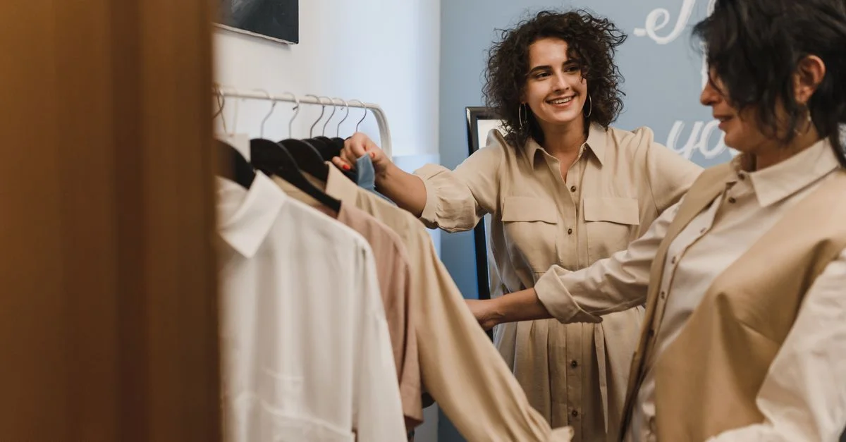 Dos mujeres disfrutando de una experiencia de compras en una moderna boutique de moda, riendo y sonriendo.