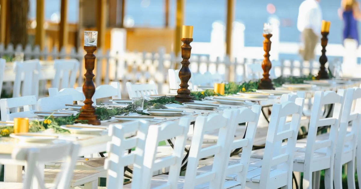 Hermosa recepción de boda al aire libre con sillas blancas y mesas decoradas junto al mar.