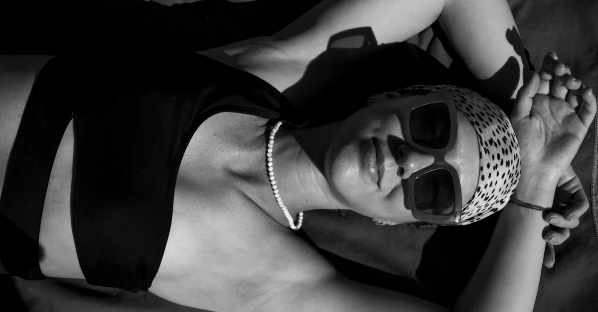 Impresionante retrato en blanco y negro de una mujer tomando el sol, usando gafas de sol y un pañuelo en la cabeza.