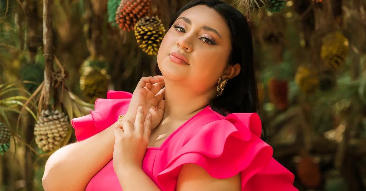 Retrato de una mujer con un vestido rosa vibrante rodeada de naturaleza.