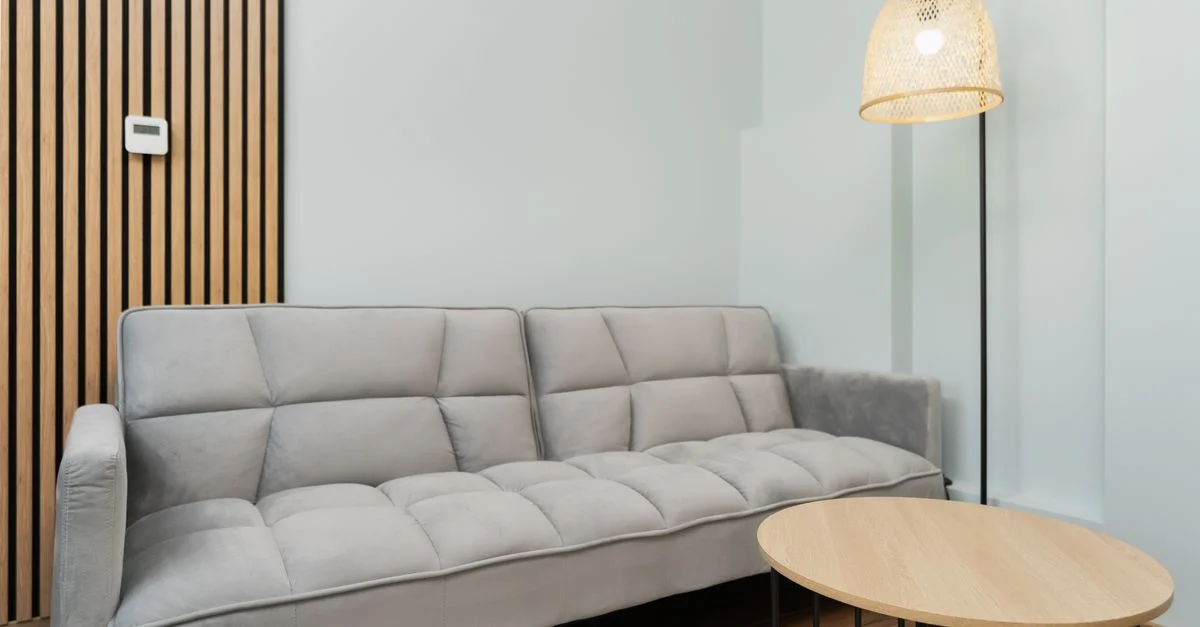 Sala de estar contemporánea con un sofá gris, detalles de madera y una lámpara tejida para una apariencia minimalista.