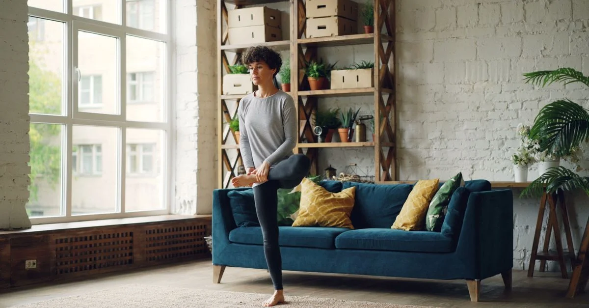 Una mujer practicando yoga en una sala de estar elegante llena de plantas.