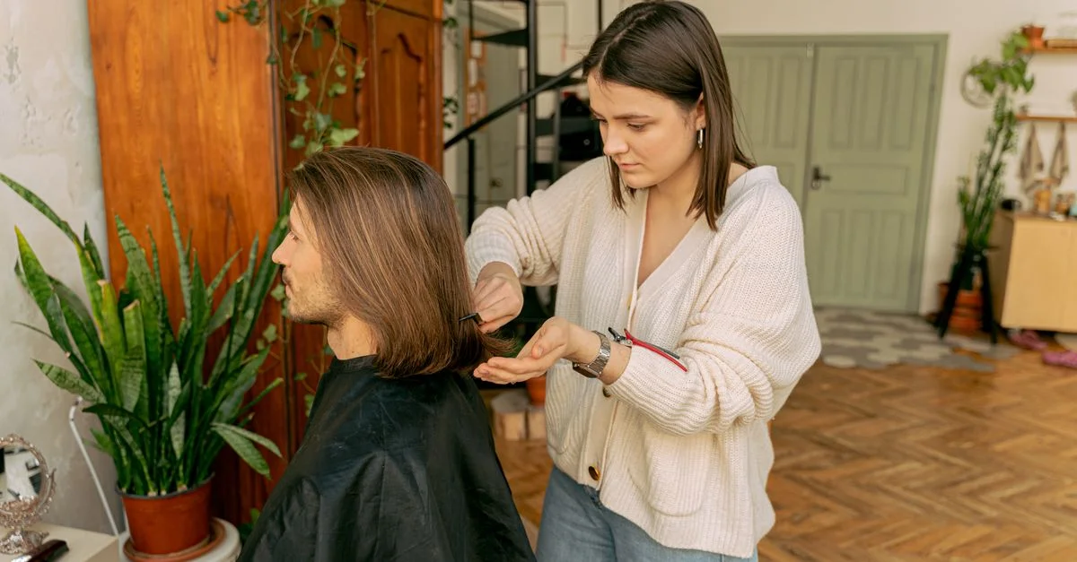 Una estilista mujer corta el cabello de un hombre en una habitación decorada cálidamente, mostrando un ambiente de salón interior.