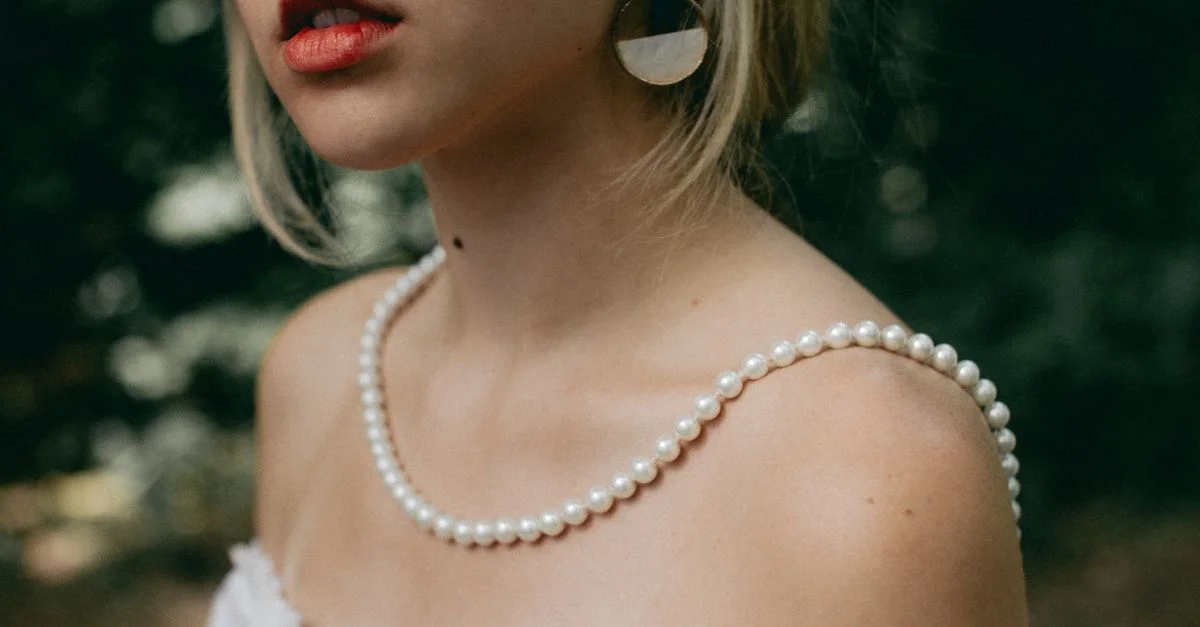 Retrato elegante en primer plano de una mujer con collar de perlas y pendientes elegantes, vistiendo un vestido blanco.