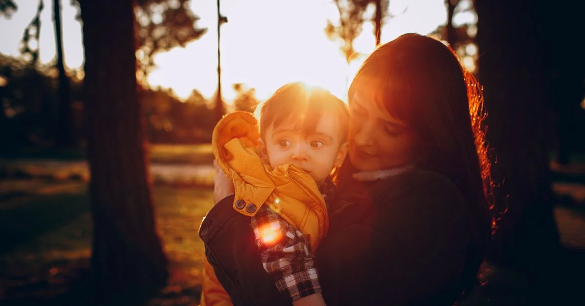 Un momento tierno entre madre e hijo en un bosque de otoño iluminado por el sol, que captura calidez y amor.