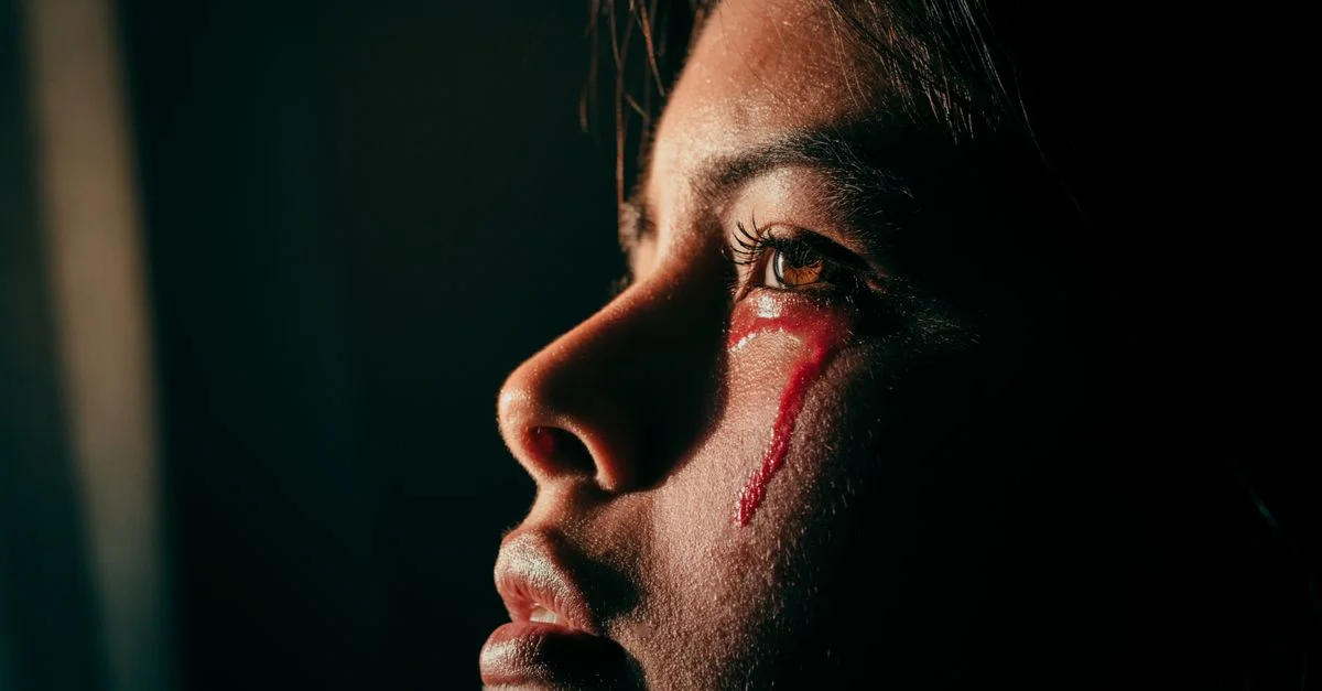 Primer plano de una mujer con luz artística y líquido rojo que asemeja lágrimas, evocando emoción y tristeza.