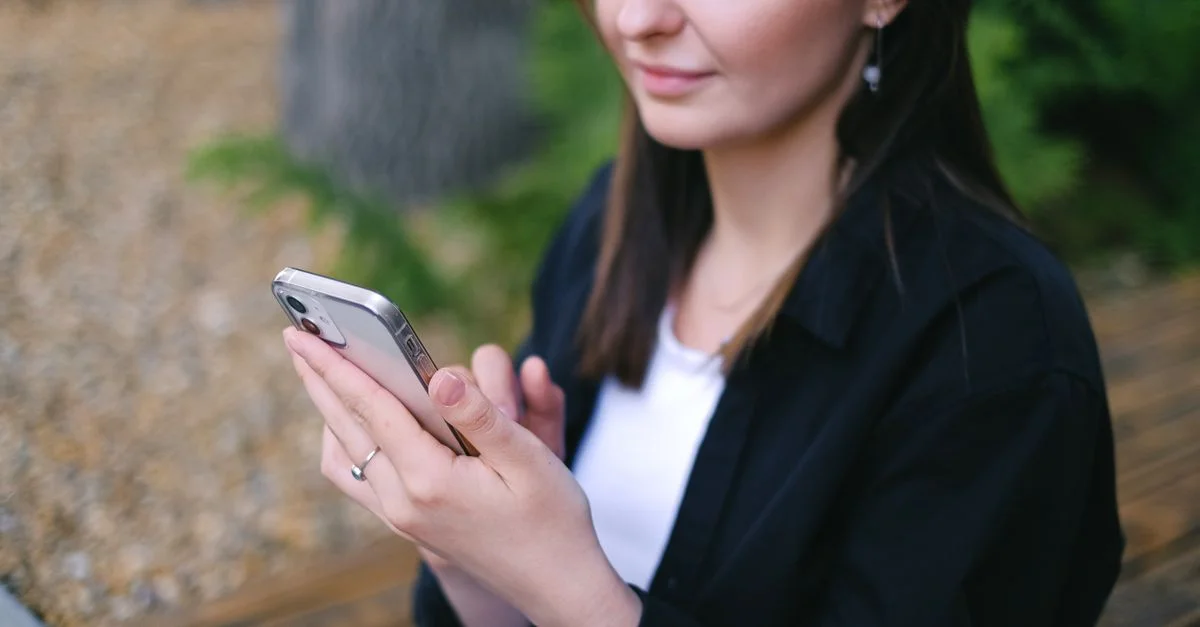 Mujer usando un teléfono inteligente al aire libre, disfrutando del ocio y la relajación.