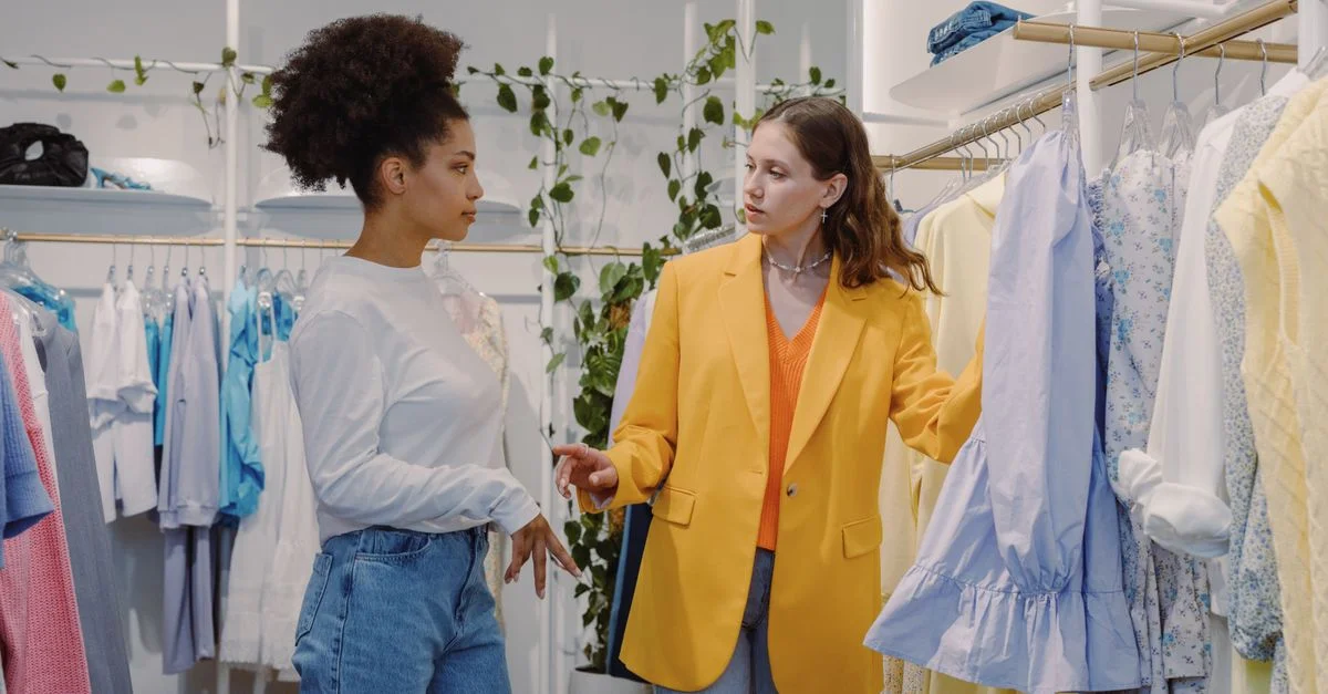 Dos mujeres en una tienda de moda revisando ropa, discutiendo estilos.