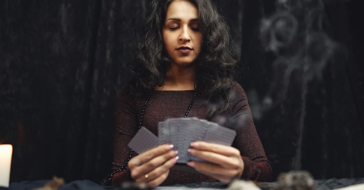Una mujer participando en una sesión espiritual de lectura de cartas con velas, humo y cristales.