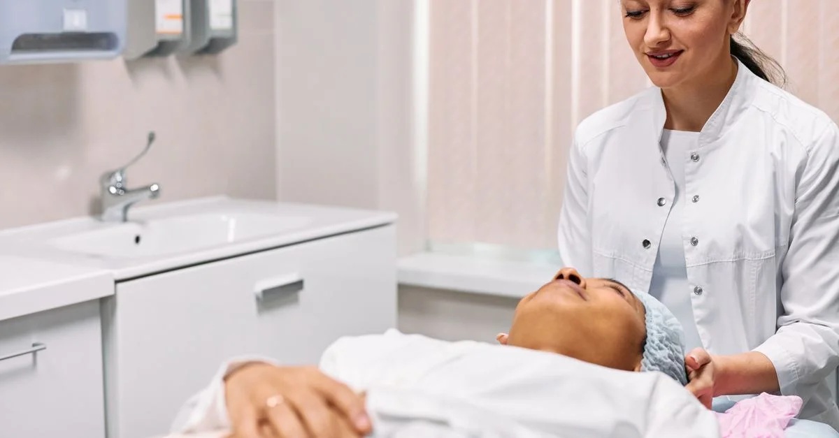 Una esteticista proporcionando tratamiento facial a una mujer en un entorno clínico, con énfasis en el cuidado y la relajación.