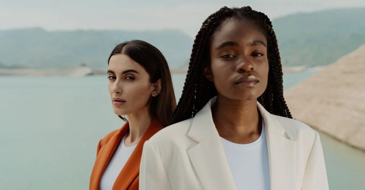 Retrato elegante de dos mujeres a la moda en trajes junto a un lago sereno, irradiando confianza y estilo.
