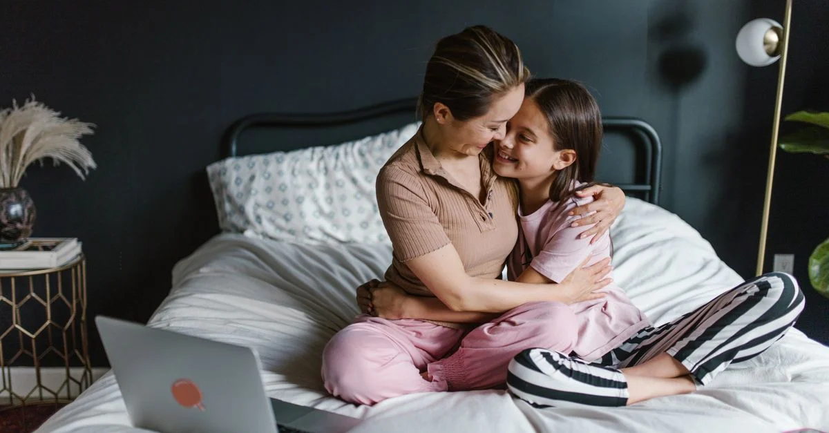 Una madre y su hija se abrazan en la cama, compartiendo un momento cálido en casa.