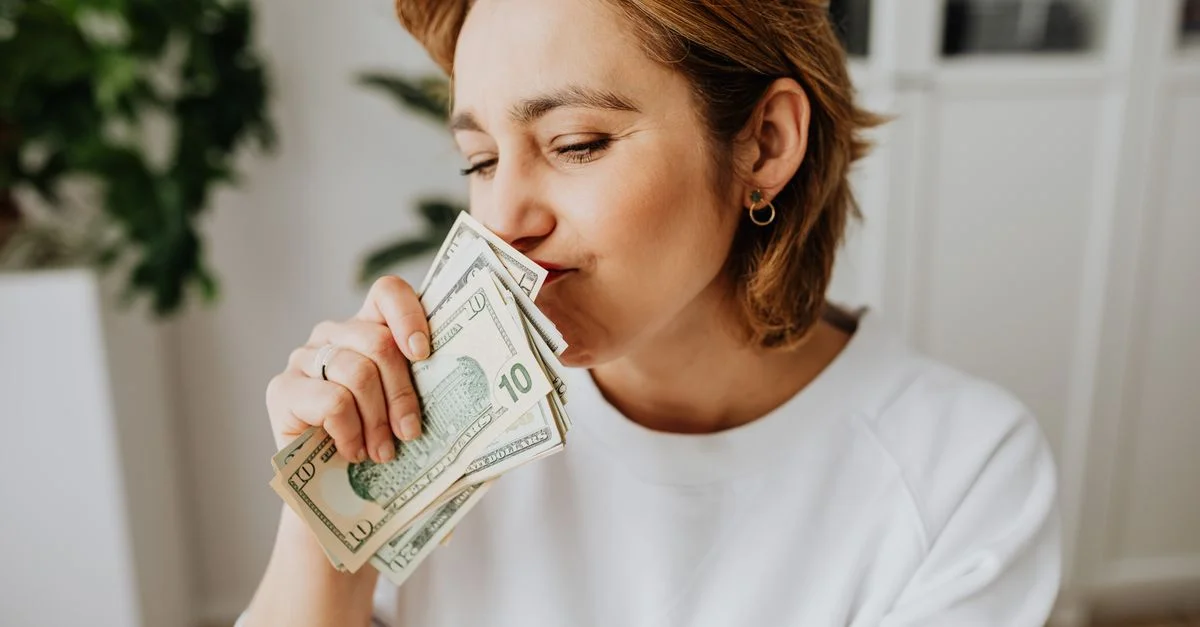 Una mujer oliendo alegremente un puñado de billetes de dólar estadounidenses en el interior.