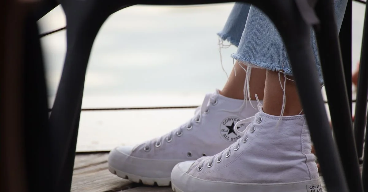 Zapatillas blancas casuales y jeans desgastados en un ambiente exterior con una terraza de madera.