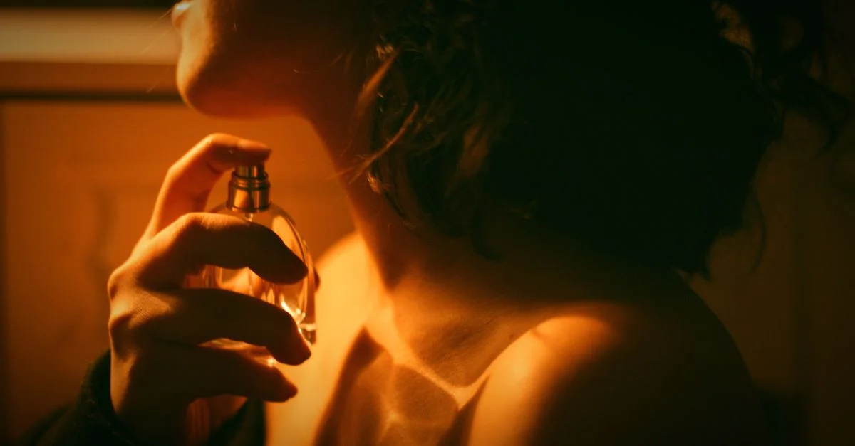 Primer plano artístico de una mujer aplicándose perfume con luz cálida.