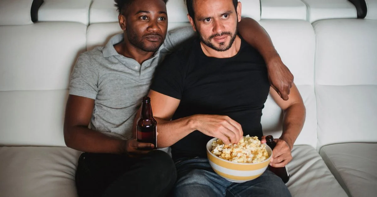 Una cariñosa pareja interracial disfrutando de una noche de película en el sofá con palomitas y bebidas.