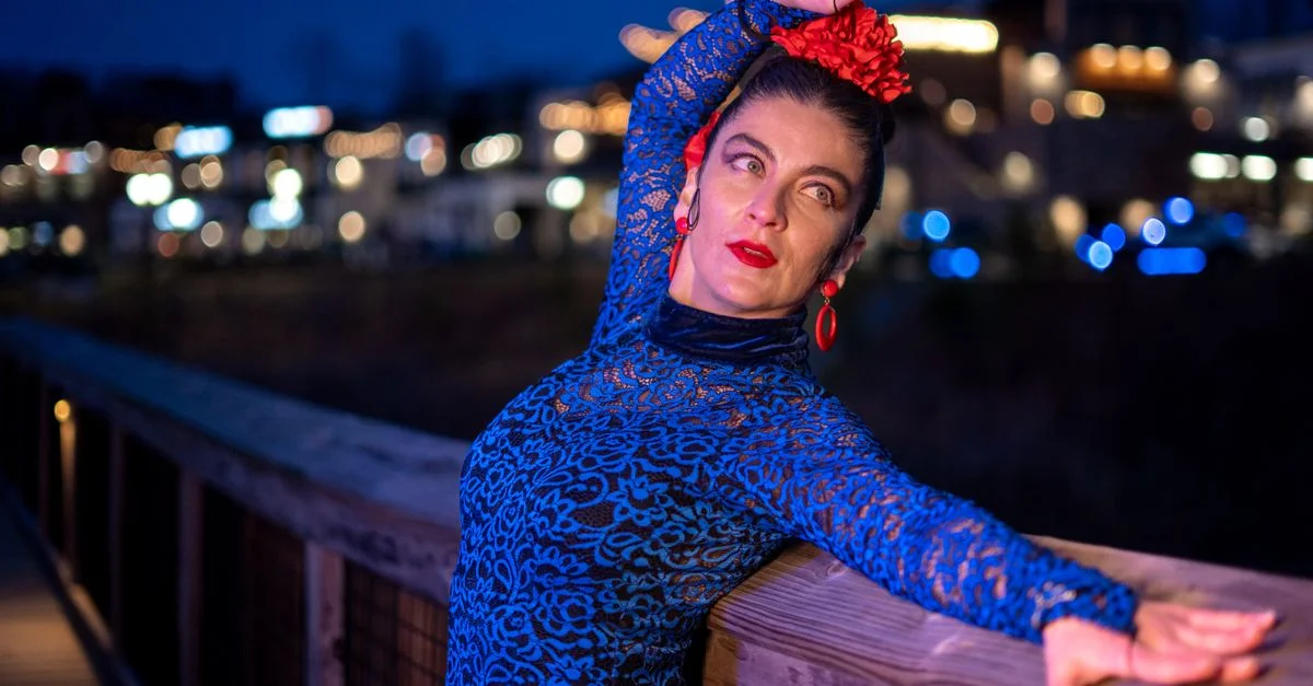 Bailarina de flamenco posa con vestido vibrante en un paseo iluminado tenue.