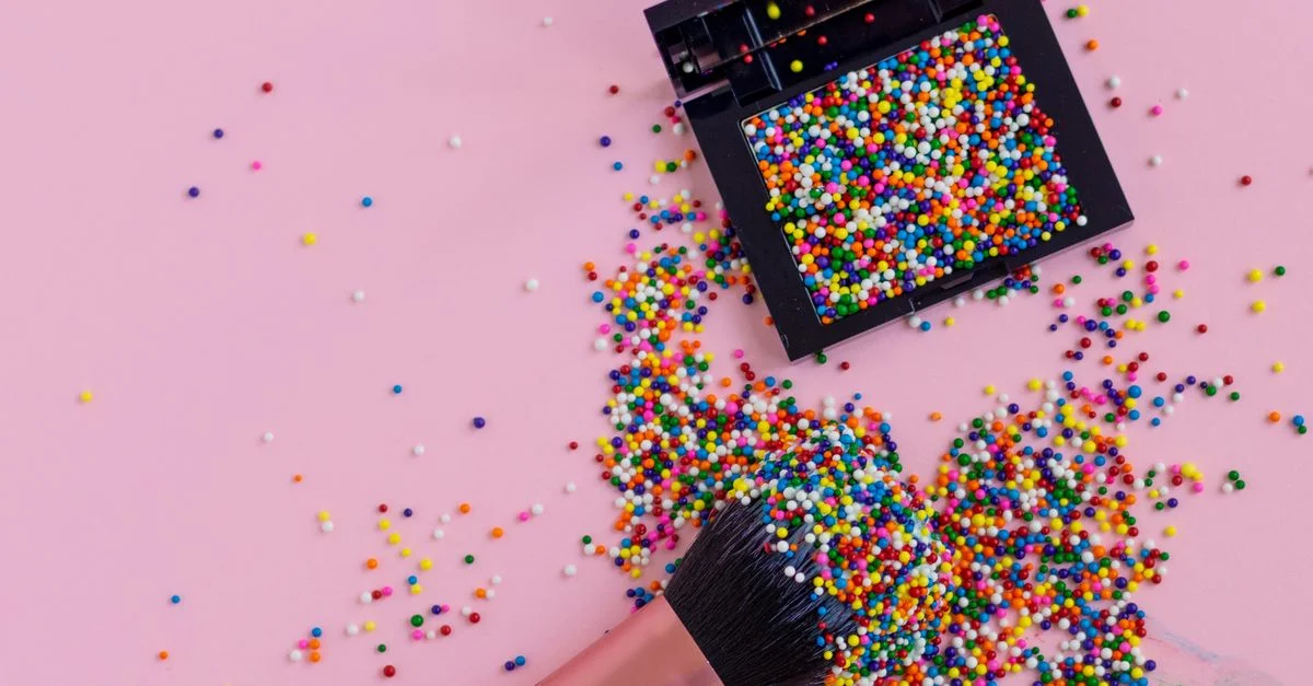 Una brocha de maquillaje con decoraciones vibrantes sobre un fondo rosa, realzando temas de belleza creativa.