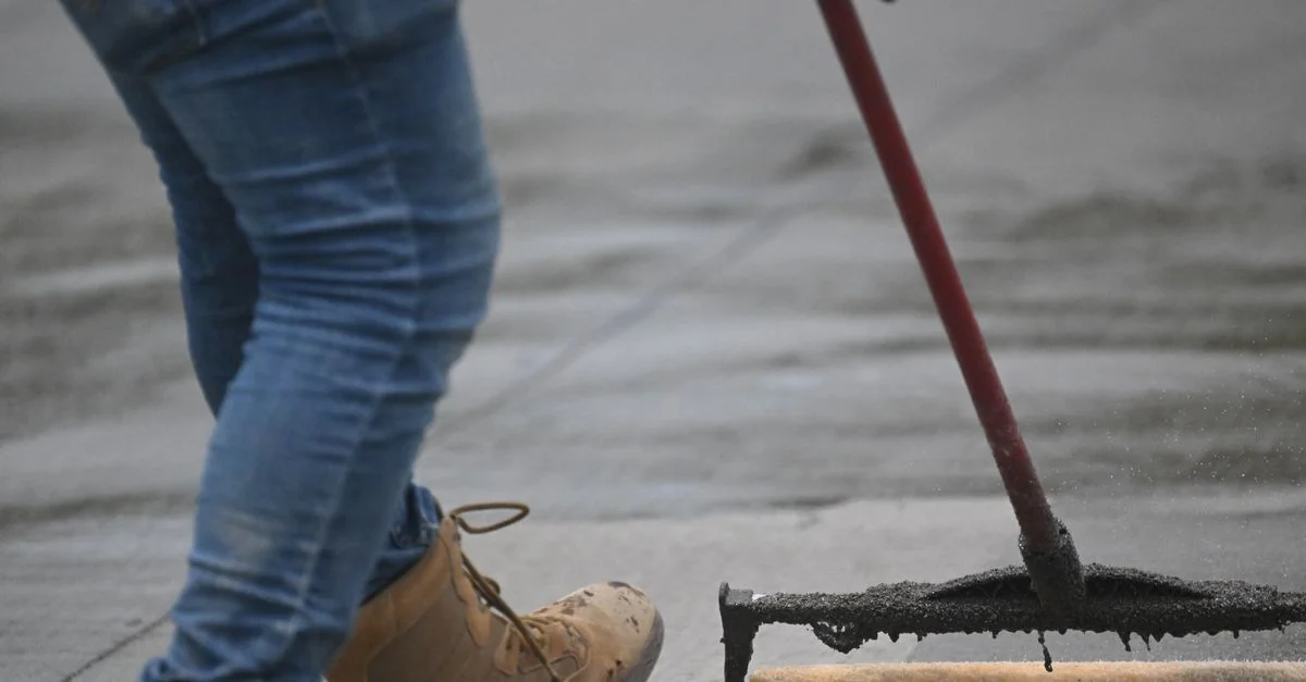 Imagen detallada del sellado de concreto con un rodillo sobre el pavimento, mostrando botas y jeans en acción.
