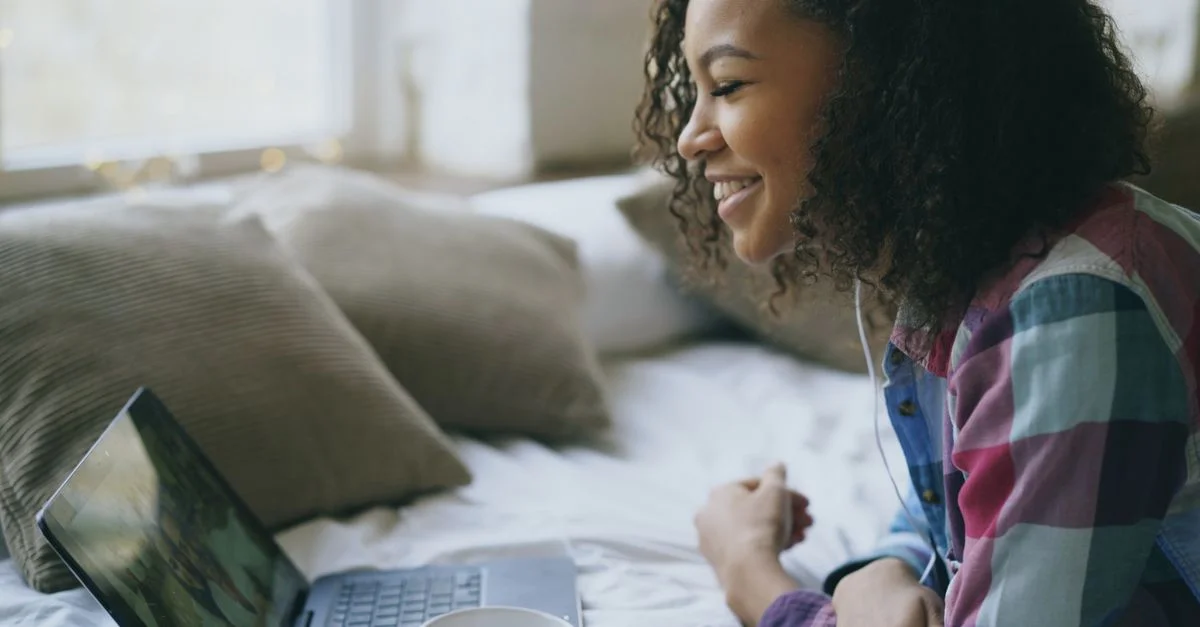 Joven mujer sonriendo usando una laptop en un ambiente interior acogedor, disfrutando de la interacción online.