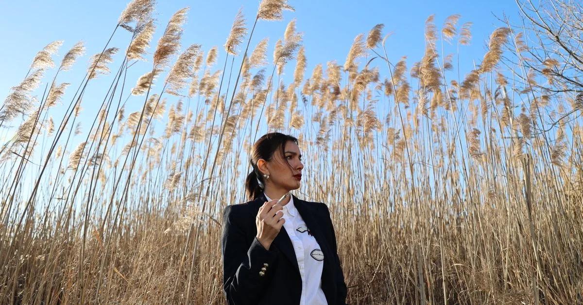 Mujer elegante con traje de negocio de pie entre hierba de pampos bajo un cielo azul claro.