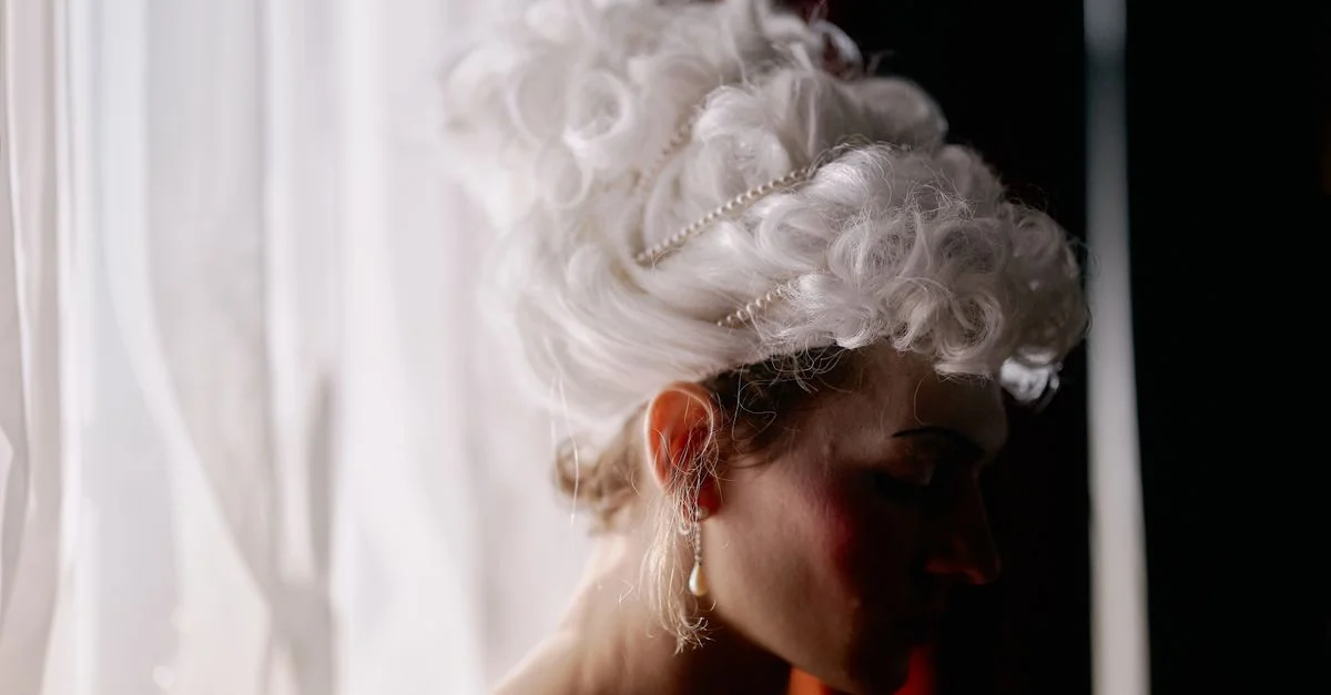 Una mujer con una peluca aristocrática mira por la ventana, capturando un momento de elegancia intemporal.