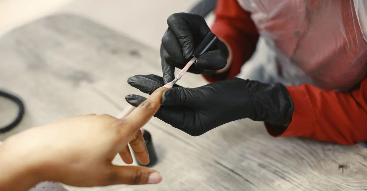 Una artista de uñas aplica cuidadosamente esmalte a las uñas de una clienta en un entorno de salón, utilizando técnicas precisas.