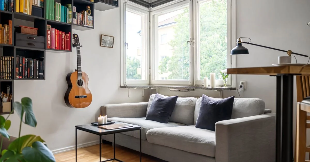Sala de estar estilosa con estanterías, una guitarra clásica y un sofá cómodo junto a grandes ventanas.