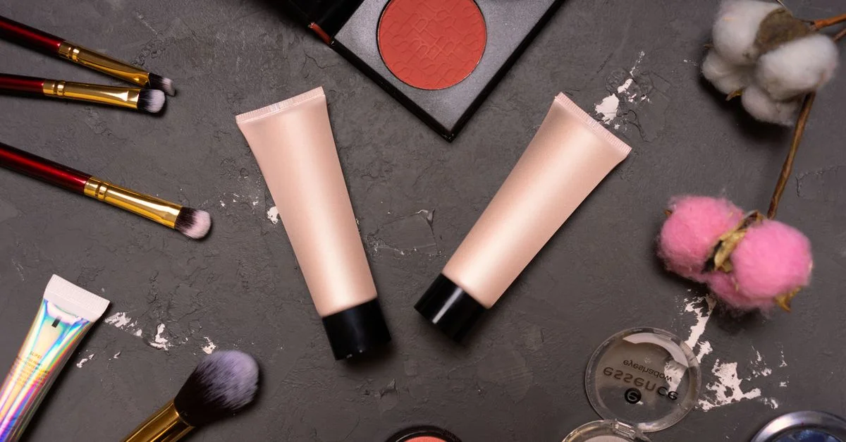 Un flat lay elegante que presenta cosméticos, incluyendo brochas y cremas sobre un fondo oscuro.