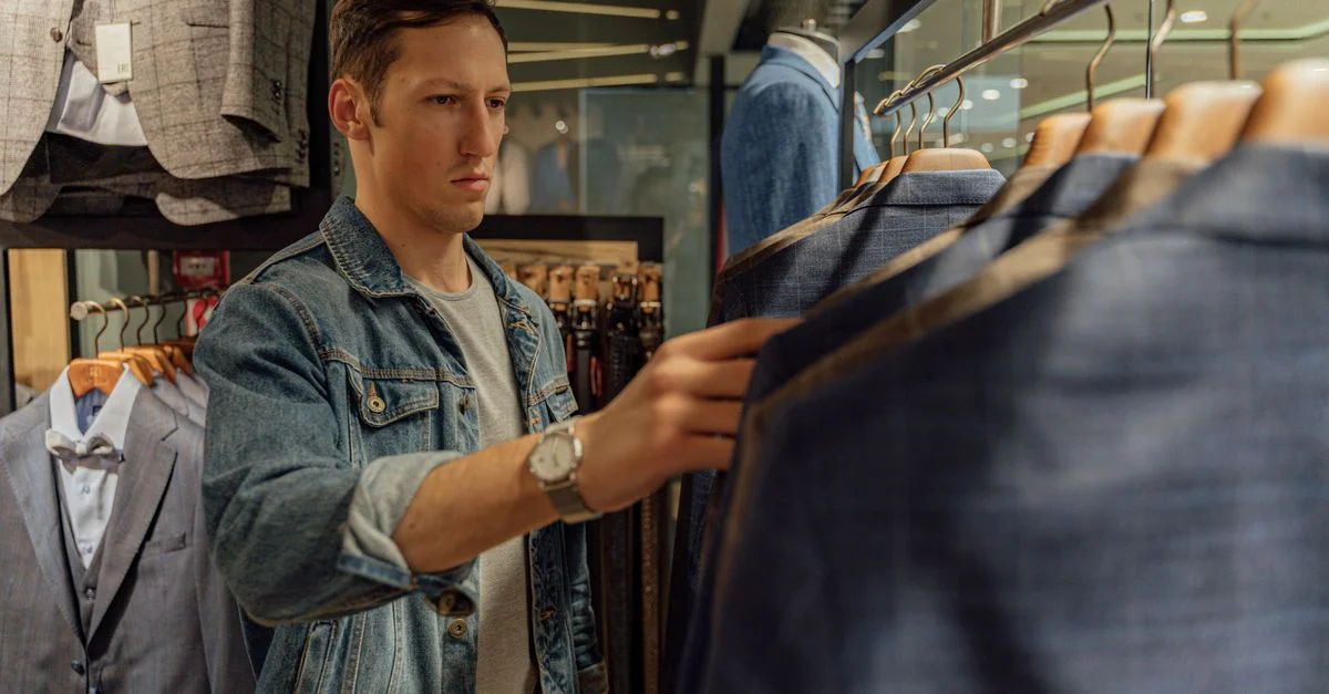 Joven viendo trajes en una tienda de ropa, seleccionando un nuevo atuendo.