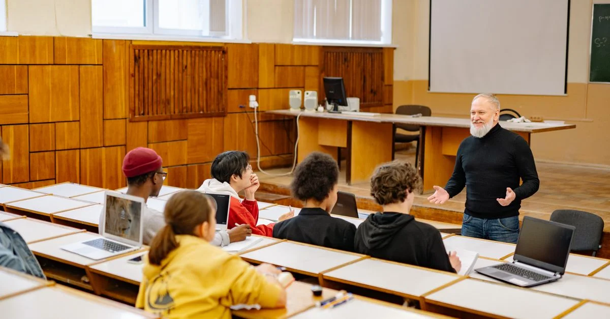 Estudiantes interactuando con un profesor en un aula universitaria, utilizando tecnología.