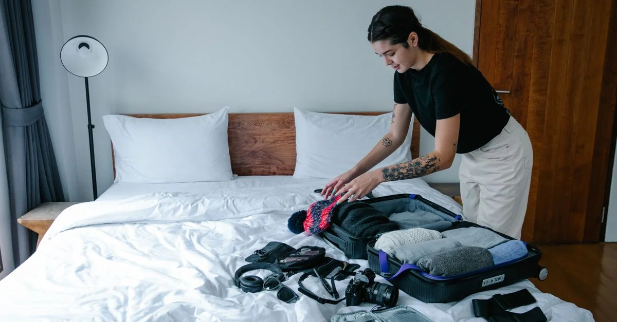 Mujer joven organizando equipaje en una cama en un entorno interior elegante, preparándose para viajar.
