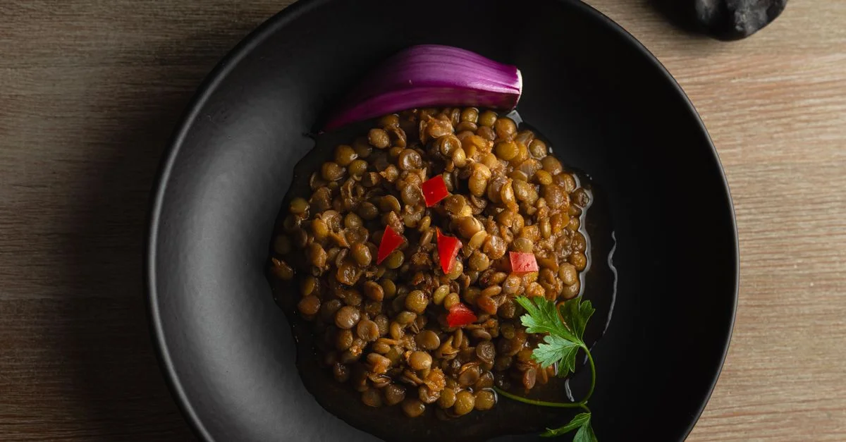 Vista superior de un plato sabroso de lentejas adornado con cebolla y perejil en un tazón negro.