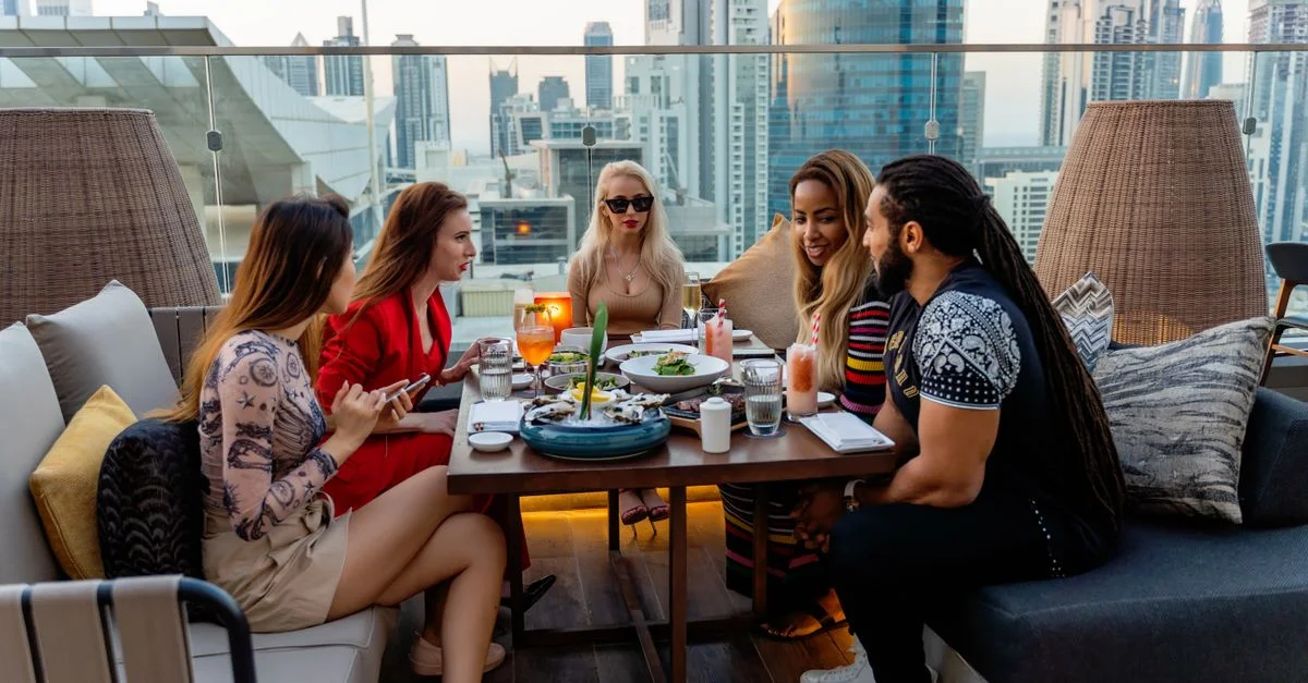 Grupo de amigos cenando en una terraza en la azotea con una impresionante vista del horizonte de Dubái.
