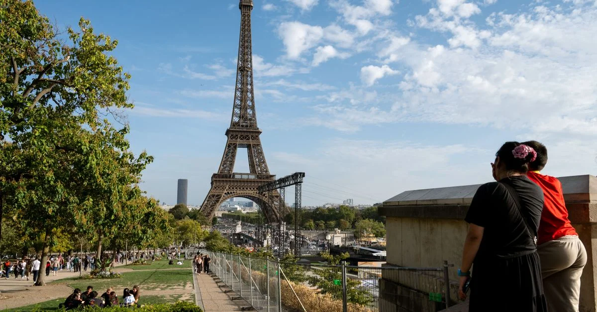 Los turistas disfrutan de un día soleado en París, contemplando la emblemática Torre Eiffel desde un parque cercano.