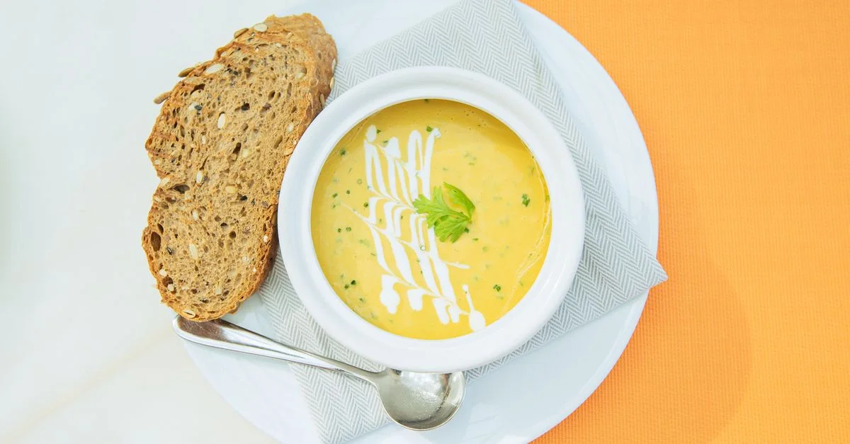 Un cuenco de sopa cremosa de verduras adornada con crema y hierbas, servida con pan artesanal.