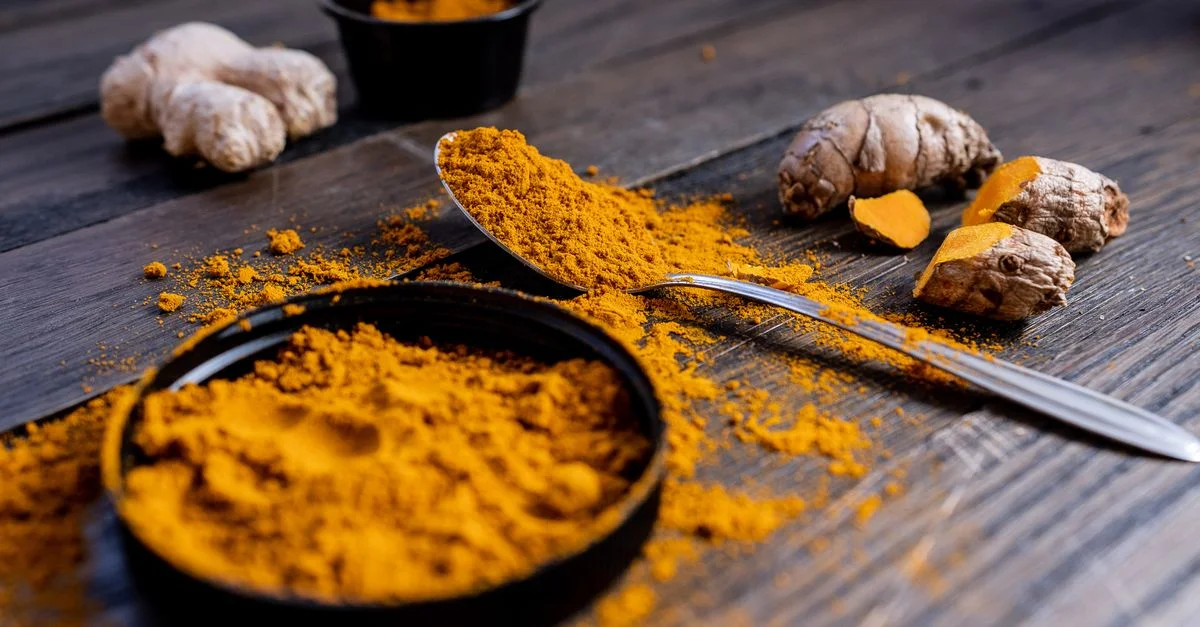 Pó de cúrcuma vibrante y raíz dispuestos sobre una superficie de madera rústica, exhibiendo ingredientes de especias culinarias.