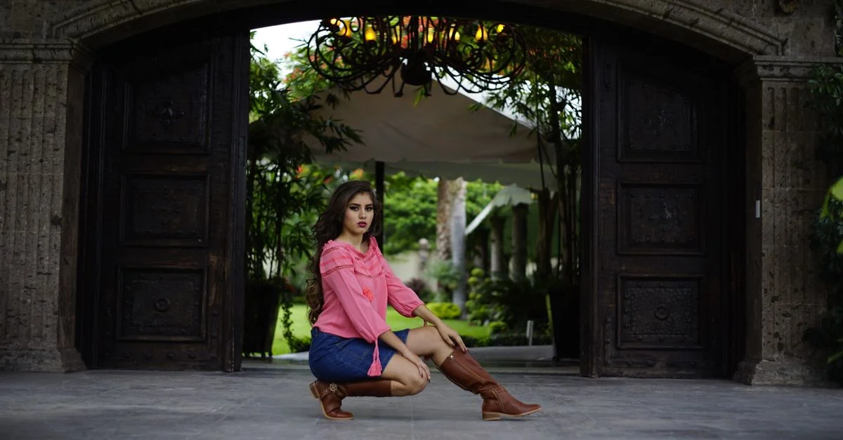 Mujer con estilo en un top rosa y botas de vaquero posa con confianza al aire libre en un entorno elegante.
