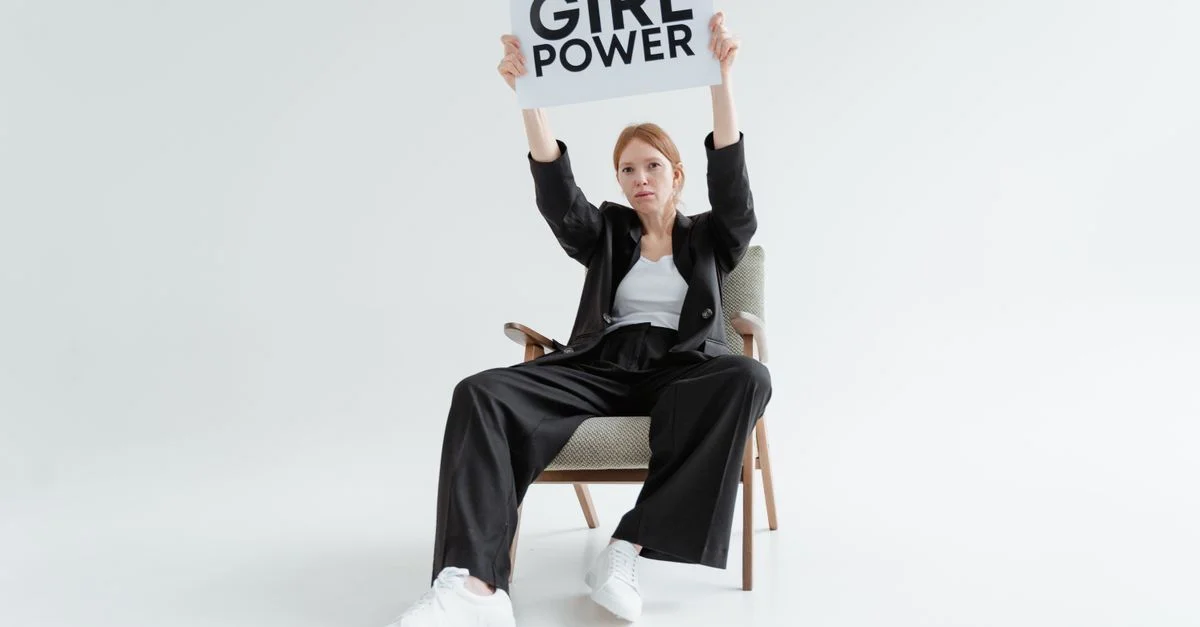 Mujer segura sentada sosteniendo un cartel de 'Girl Power' sobre un fondo blanco.