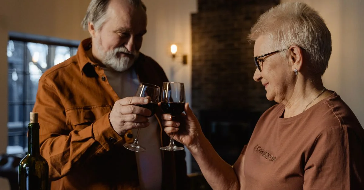 Una feliz pareja de ancianos brindando con vino tinto, disfrutando de un momento acogedor juntos.